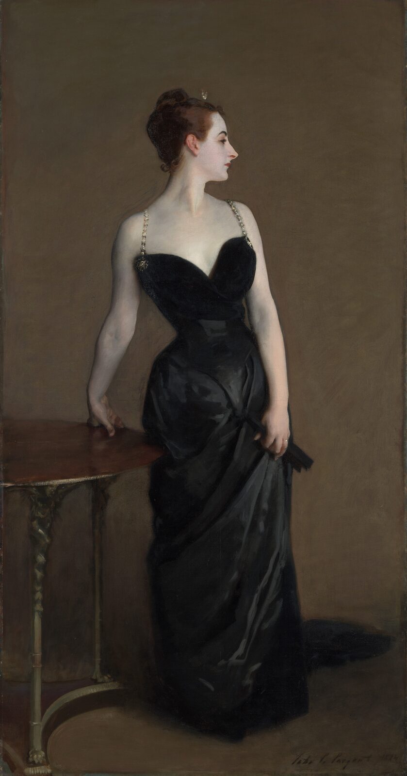 A woman in a black satin gown standing with her head turned in profile, one hand on a table