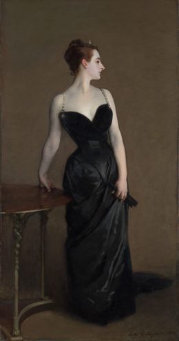 A woman in a black satin gown standing with her head turned in profile, one hand on a table